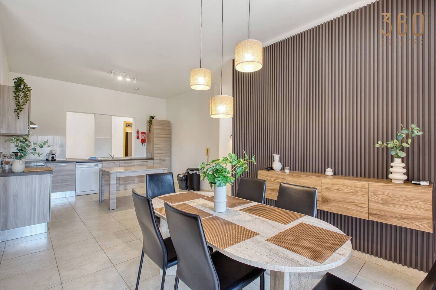 A modern kitchen with a central island, dining area with a round table, and a wooden accent wall with vertical lines.