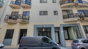 Un immeuble à plusieurs étages doté de balcons, d’une entrée au niveau du sol et d’une enseigne indiquant le nom « Kunsill Lokali San Gilian ».