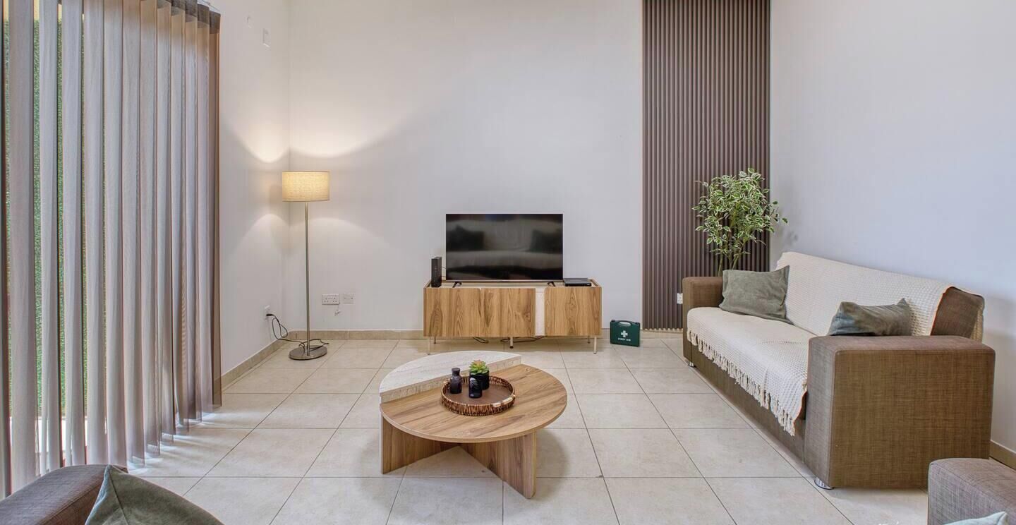 A modern living room with a flat-screen TV, a wooden coffee table, a sofa, and a floor lamp.