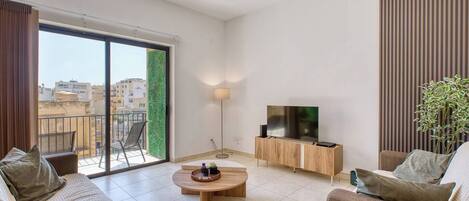 A modern living room with a sofa set, a coffee table, a TV on a wooden cabinet, and a large sliding glass door leading to a balcony.