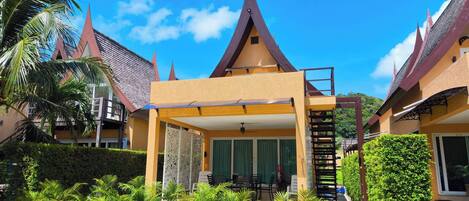 A hotel with a traditional architectural style, featuring a central atrium with a staircase, surrounded by lush greenery and palm trees.