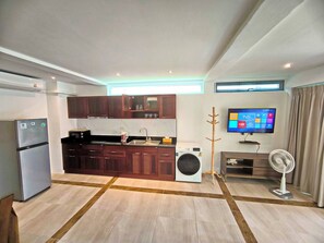 Eine moderne Küche mit dunklen Holzausführungen, einer eingebauten Mikrowelle und einer Waschmaschine. An der Wand ist ein Flachbildfernseher angebracht, und auf dem Boden steht ein kleiner Ventilator.