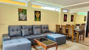 Uma sala de estar moderna com um sofá seccional, uma mesa de centro de vidro e uma área de jantar com cadeiras de madeira.