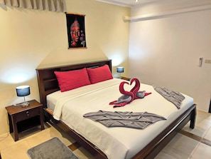 A hotel room with a bed, pillows, a bedside table with a lamp, a wall-mounted artwork, and a door.
