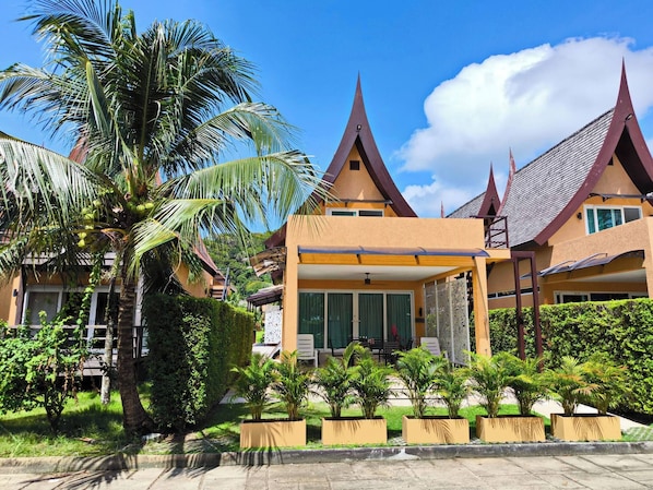 A traditional-style building with multiple roofs, a covered patio area, and lush greenery including palm trees. - 1 Bedroom Villa With Beach View Koh Chang (Ko Chang)