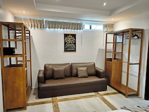 A living room with a brown leather sofa, wooden shelving units, and a wall-mounted artwork.