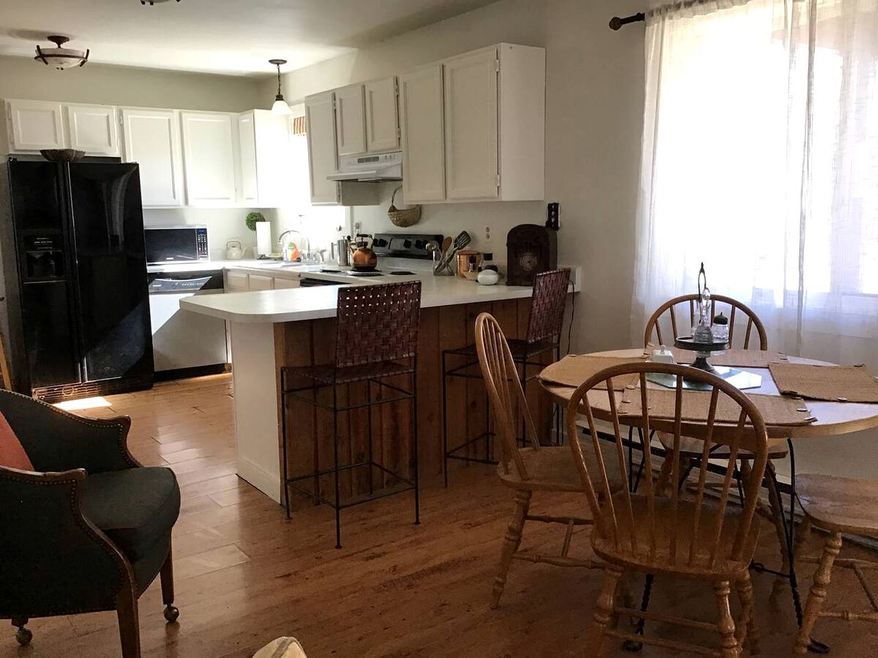 A kitchen with white cabinets, a black refrigerator, and a dining area with wooden chairs and a table.