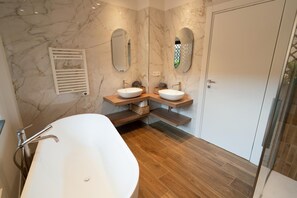 A modern bathroom with a freestanding bathtub, two vanity sinks, and marble walls. - Charming Catania Apartment With Private Entrance and Balcony (Catania)