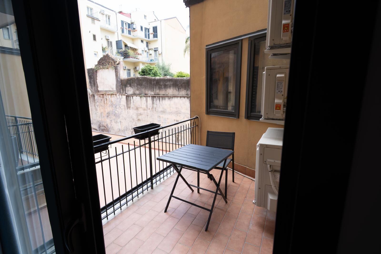 A balcony with a table and chairs, a window, and a wall-mounted air conditioning unit.