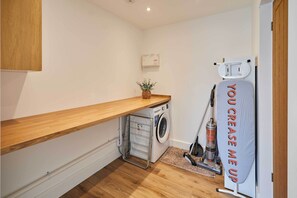 A compact laundry room with a washing machine, a drying rack, and a vacuum cleaner. - Host & Stay | Sandmoor (Whitby)