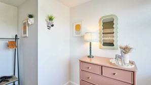 Una stanza con una rastrelliera metallica verde, un comò rosa e decorazioni a parete tra cui un vaso a forma di zebra e un quadro astratto incorniciato.