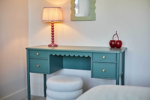 A teal-colored desk with two drawers and a round stool, a lamp, and a mirror on the wall. - Host & Stay | Sandmoor (Whitby)