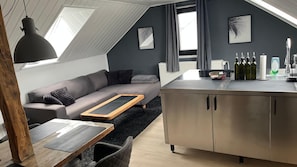 Un moderno spazio abitativo in stile loft con divano grigio, tavolino in legno e angolo cottura con pensili in acciaio inossidabile e piano di lavoro.