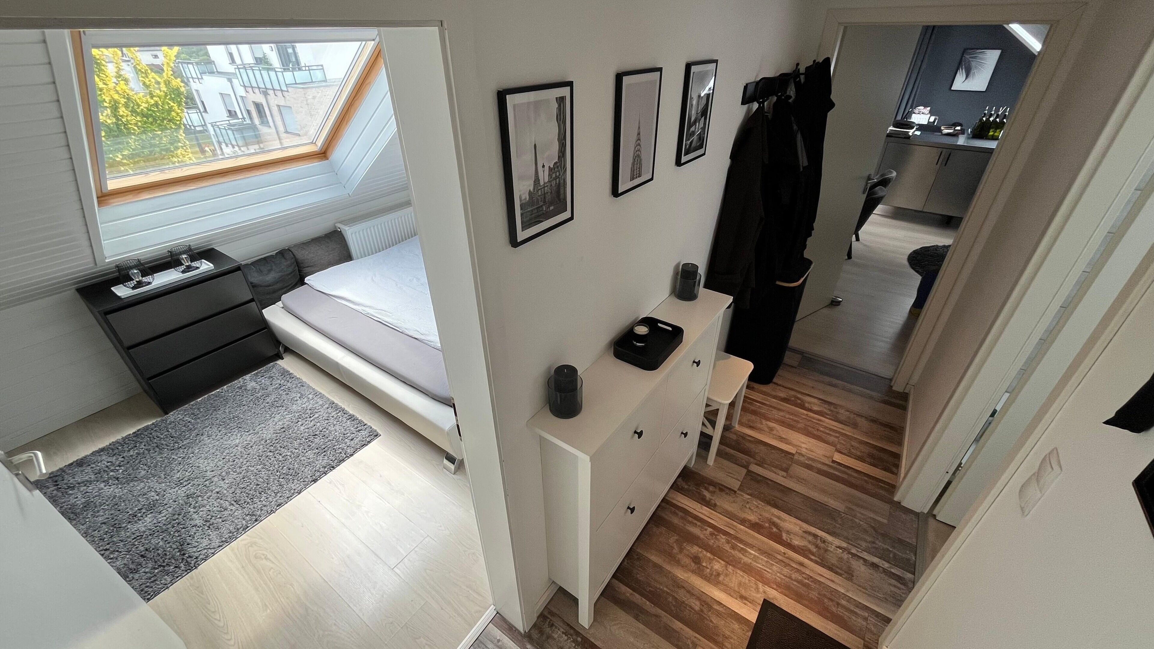 Een kleine slaapkamer met dakraam, nachtkastje, een klein dressoir en uitzicht op de aangrenzende keuken.