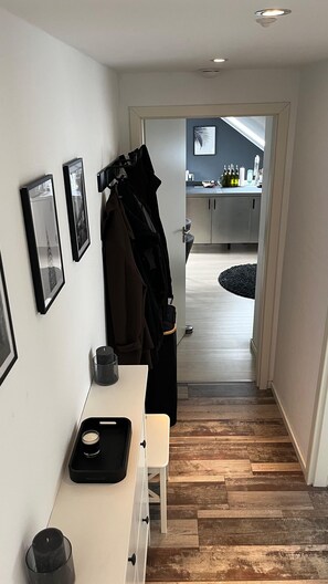 Un passadís amb una banca blanca, un penjador amb un abric i una porta que dona a una zona de cuina.