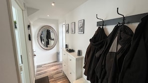 Un corridoio con un appendiabiti, uno specchio con cornice decorativa, un armadietto bianco e una porta che conduce a un'altra stanza.