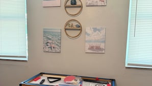 A room with a foosball table, framed artwork on the wall, and a patterned rug. - Sleep 4 in this bright Pensacola cottage just minutes from Perdido Key's white sands and the National Naval Aviation Museum. Full kitchen, in-unit laundry, comfy queen bed, and a picnic-table yard. Your easy Gulf Coast home base awaits! (Pensacola)