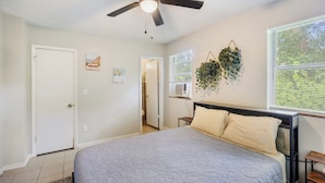 A bedroom with a bed, a ceiling fan, a window with blinds, and a wall-mounted plant. - Sleep 4 in this bright Pensacola cottage just minutes from Perdido Key's white sands and the National Naval Aviation Museum. Full kitchen, in-unit laundry, comfy queen bed, and a picnic-table yard. Your easy Gulf Coast home base awaits! (Pensacola)