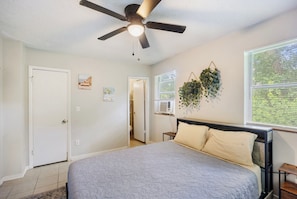 A bedroom with a bed, a ceiling fan, a window with blinds, and a wall-mounted plant. - Sleep 4 in this bright Pensacola cottage just minutes from Perdido Key's white sands and the National Naval Aviation Museum. Full kitchen, in-unit laundry, comfy queen bed, and a picnic-table yard. Your easy Gulf Coast home base awaits! (Pensacola)