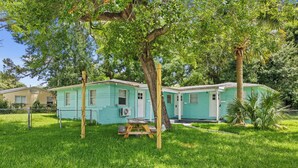 A two-story house with a green exterior, a wooden deck, and a fenced yard. - Sleep 4 in this bright Pensacola cottage just minutes from Perdido Key's white sands and the National Naval Aviation Museum. Full kitchen, in-unit laundry, comfy queen bed, and a picnic-table yard. Your easy Gulf Coast home base awaits! (Pensacola)