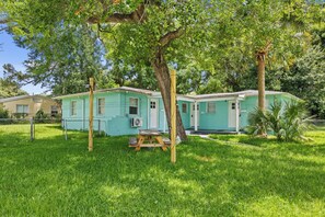 A two-story house with a green exterior, a wooden deck, and a fenced yard. - Sleep 4 in this bright Pensacola cottage just minutes from Perdido Key's white sands and the National Naval Aviation Museum. Full kitchen, in-unit laundry, comfy queen bed, and a picnic-table yard. Your easy Gulf Coast home base awaits! (Pensacola)