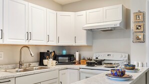 A kitchen with white cabinets, a stainless steel sink, a microwave, a stove, and a marble countertop. - Sleep 4 in this bright Pensacola cottage just minutes from Perdido Key's white sands and the National Naval Aviation Museum. Full kitchen, in-unit laundry, comfy queen bed, and a picnic-table yard. Your easy Gulf Coast home base awaits! (Pensacola)