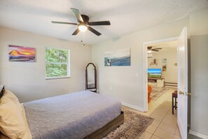 A bedroom with a bed, a ceiling fan, and artwork on the walls. - Sleep 4 in this bright Pensacola cottage just minutes from Perdido Key's white sands and the National Naval Aviation Museum. Full kitchen, in-unit laundry, comfy queen bed, and a picnic-table yard. Your easy Gulf Coast home base awaits! (Pensacola)