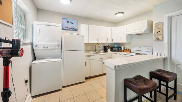 A compact kitchen with white appliances, a tiled floor, and a small bar area with stools. - Sleep 4 in this bright Pensacola cottage just minutes from Perdido Key's white sands and the National Naval Aviation Museum. Full kitchen, in-unit laundry, comfy queen bed, and a picnic-table yard. Your easy Gulf Coast home base awaits! (Pensacola)