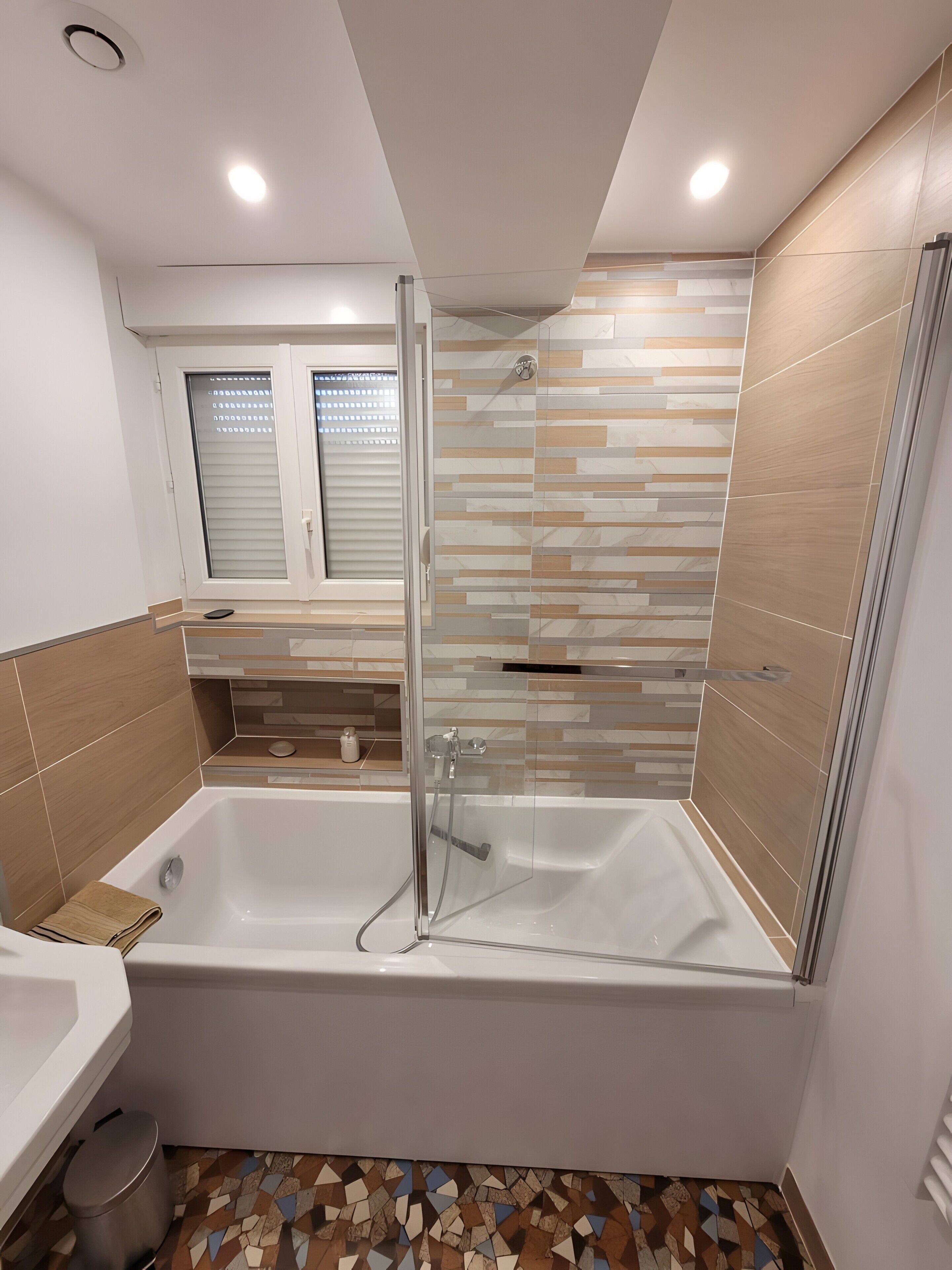 Un baño moderno con bañera, cabina de ducha y ventana con persianas.