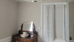 Ein Zimmer mit einem Holzkasten, einem Spiegel, einer weißen Tür mit Fenster und einer Deckenleuchte.