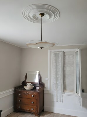 A room with a wooden dresser, a mirror, a white door with a window, and a ceiling light fixture.