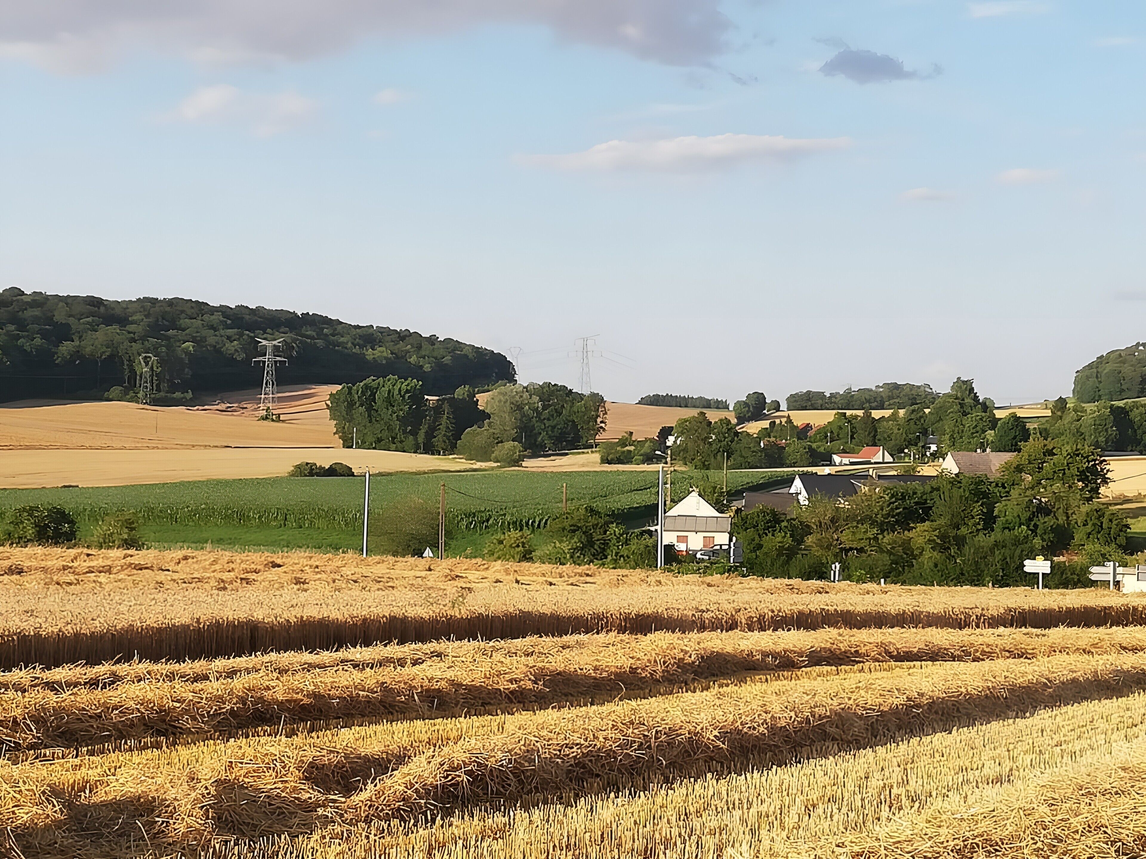 Paisaje rural con campos, un pequeño edificio blanco y una colina al fondo.