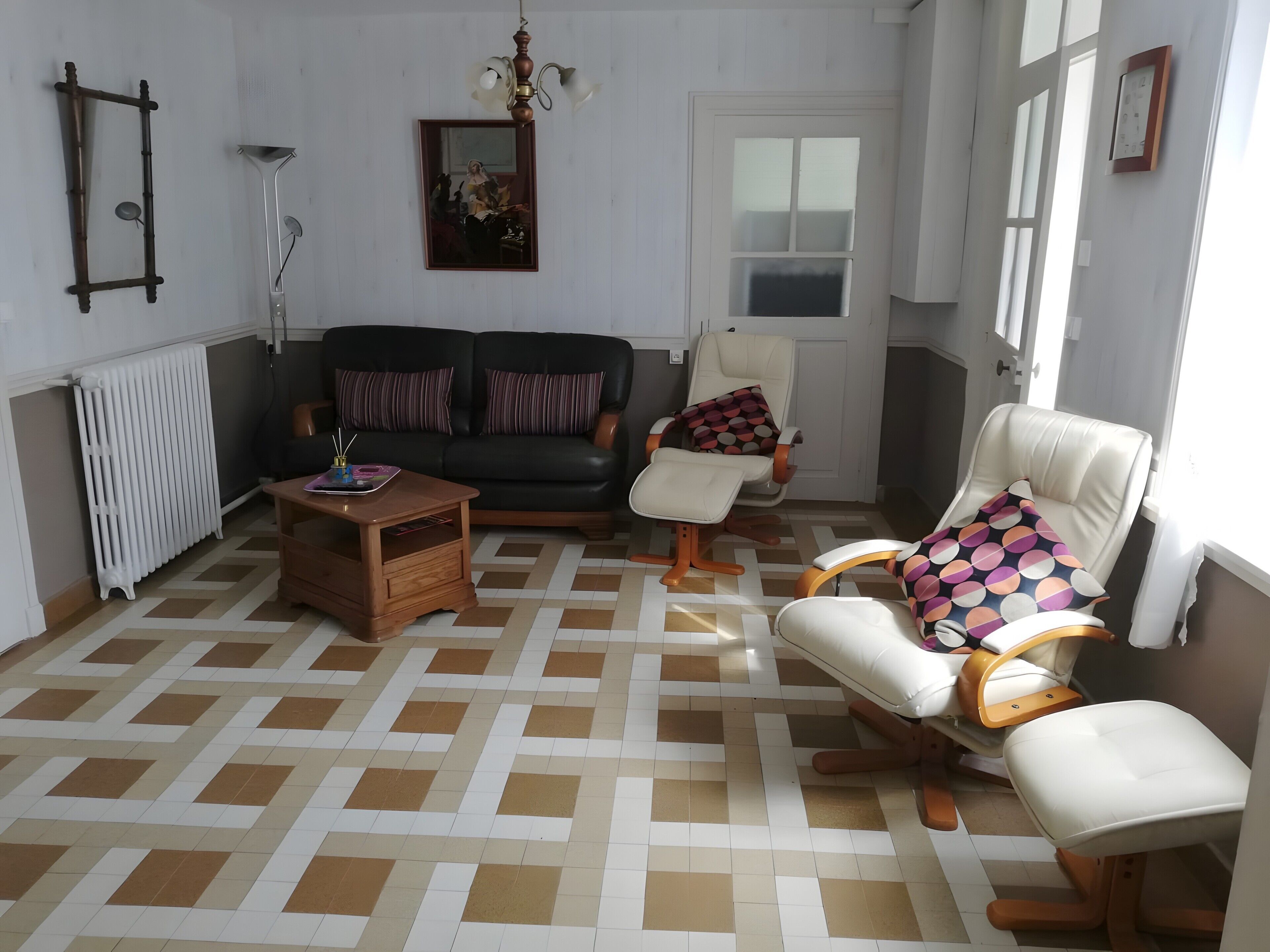 Uma sala de estar com sofá, duas poltronas, uma mesa de centro, um radiador e uma janela com cortinas.