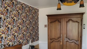 Ein Schlafzimmer mit einem Bett, einem Holzschrank, einem Wandpapier mit Muster und einer Deckenleuchte.