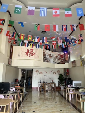 Et hotellobby med flere borde og stole, en reception og en stor dekorativ banner med flag.
