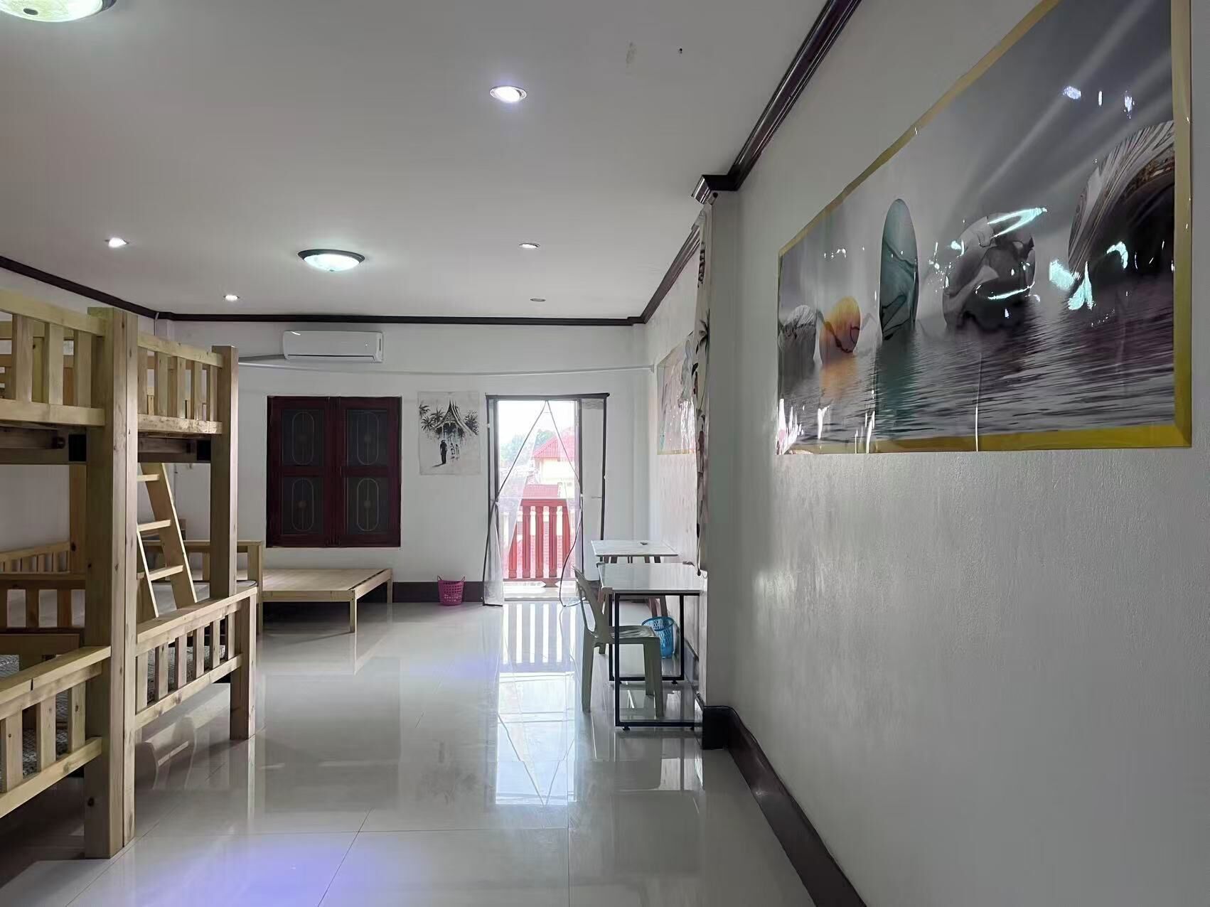 A room with a bunk bed, a desk, and a chair. There is a window with a view of a red building outside.