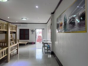 A room with a bunk bed, a desk, and a chair. There is a window with a view of a red building outside.