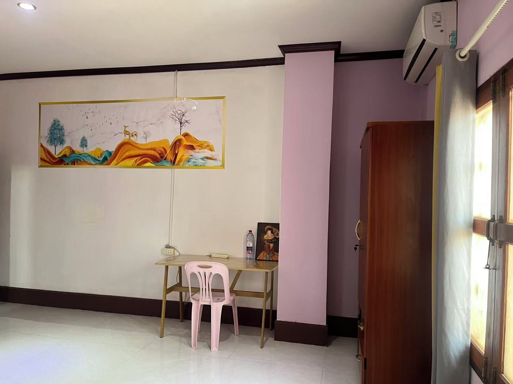 Ein Zimmer mit Esstisch, einem rosa Stuhl, einem Bild an der Wand und einer Klimaanlage.