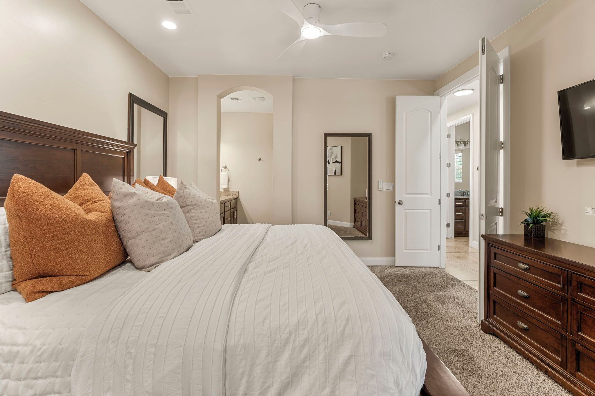 A bedroom with a large bed, a dresser, a TV, and a door leading to another room.
