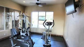 A gym with cardio machines, a television, and a large window.