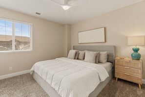 A bedroom with a bed, a nightstand, a lamp, and a window with blinds. - Cactus Rose at Coral Ridge | Sage Vacations (Washington)