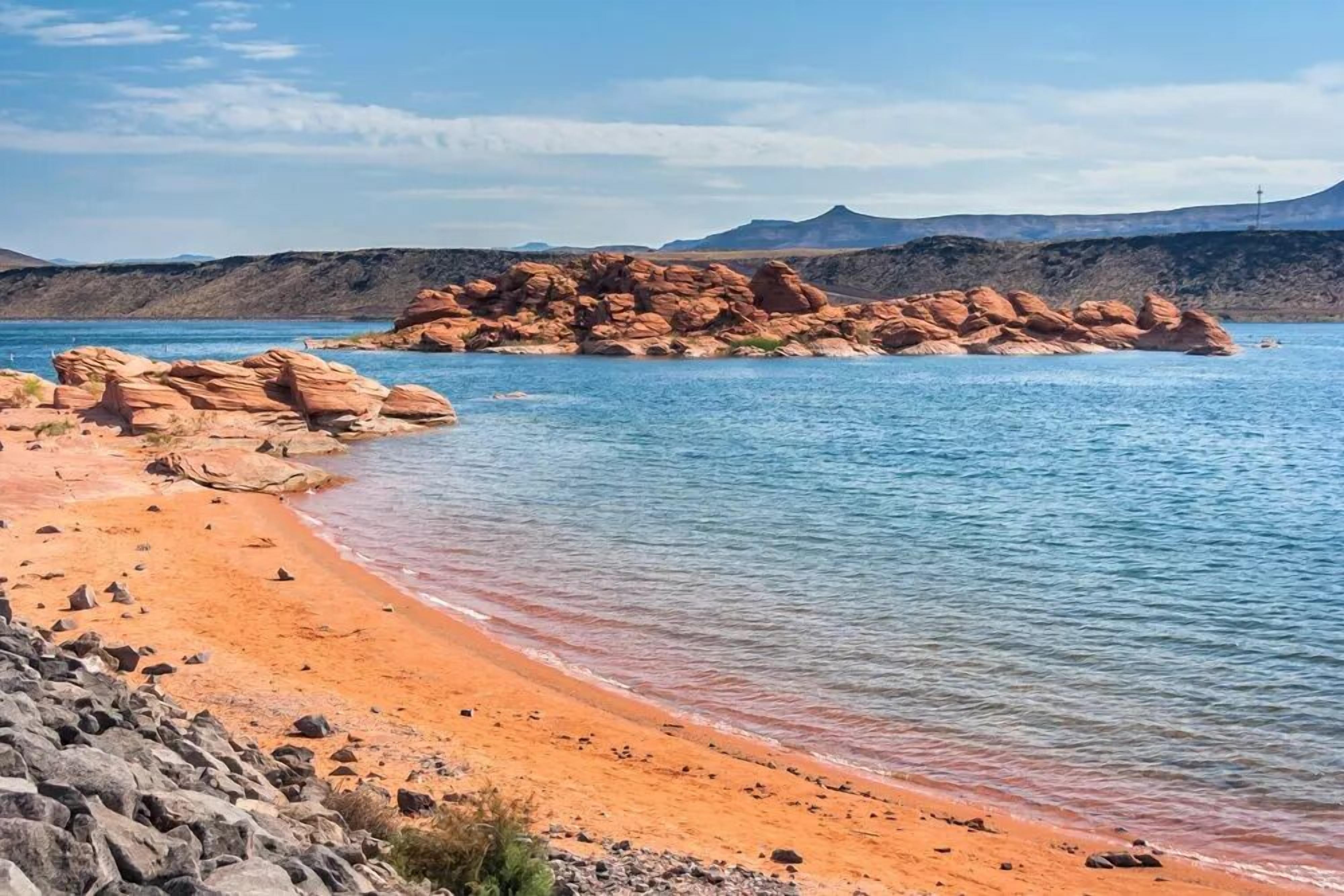 A beach with clear blue water, rocky formations, and distant mountains.