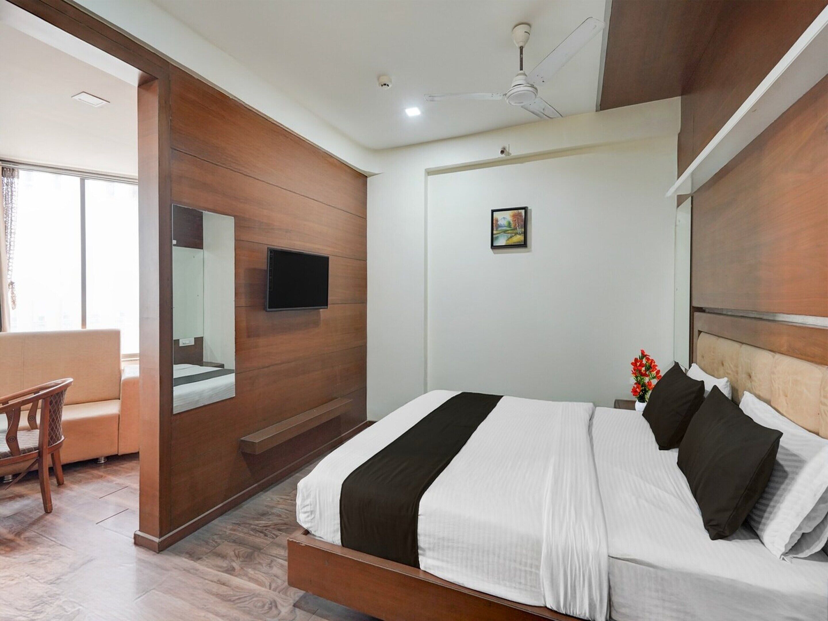 Una habitación de hotel con cama, televisión, un cuadro y ventilador de techo.