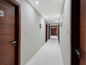 A long, narrow hotel corridor with wooden doors on either side, white walls, and a tiled floor.