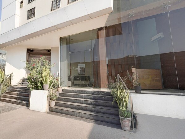 A modern building with a glass facade, a set of concrete steps leading to a door, and potted plants on either side.