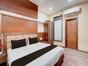 A hotel room with a large bed, wooden headboard, a wardrobe, a mirror, and an air conditioning unit. - Super Deluxe Twin Room Hotel Navjivan (Himatnagar)
