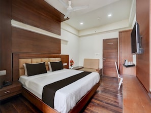 A hotel room with a large bed, wooden headboard, bedside tables, a TV, and a ceiling fan. - Super Deluxe Twin Room Hotel Navjivan (Himatnagar)