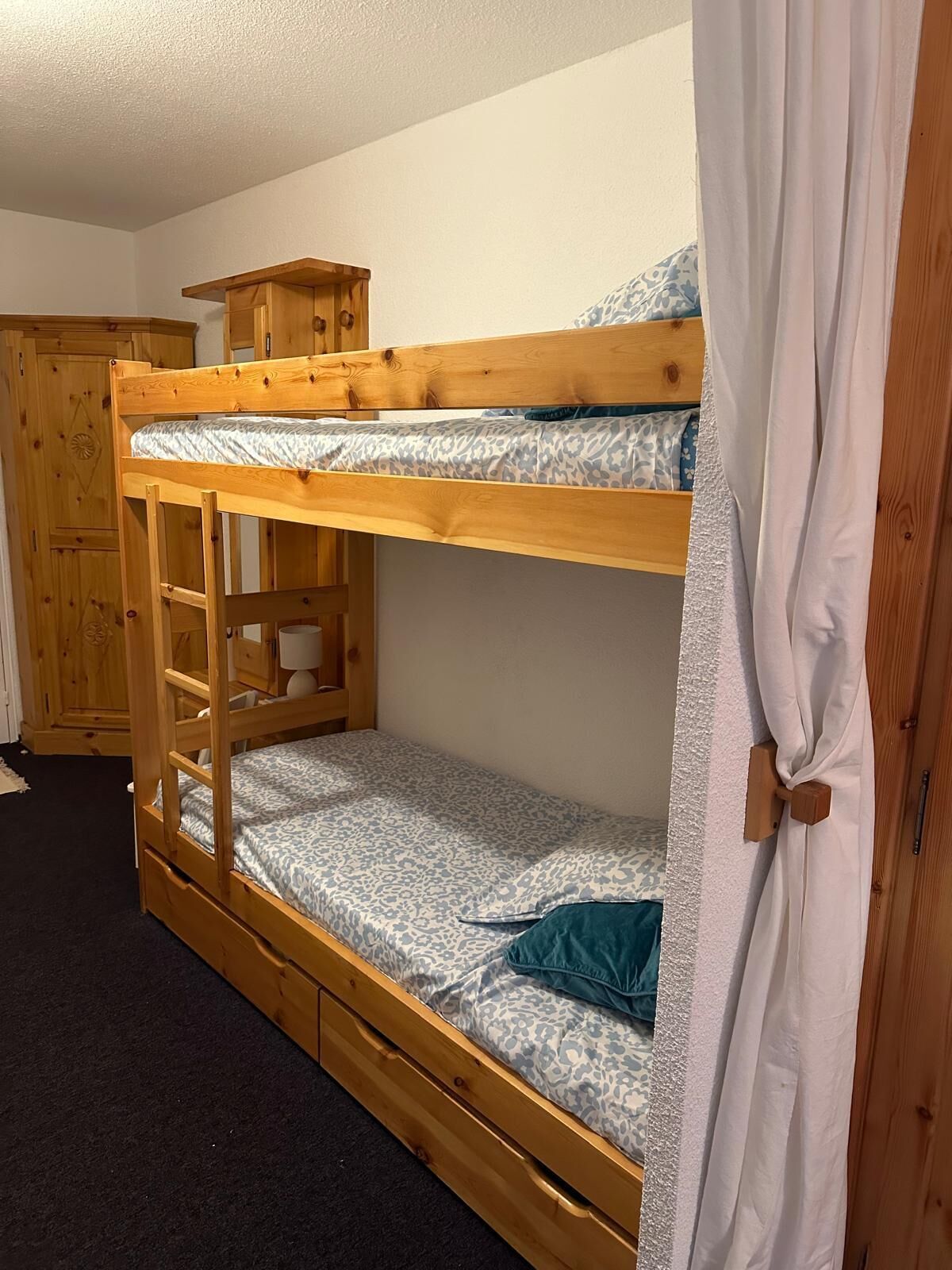 A bunk bed with a wooden frame, a small shelf, and a drawer.