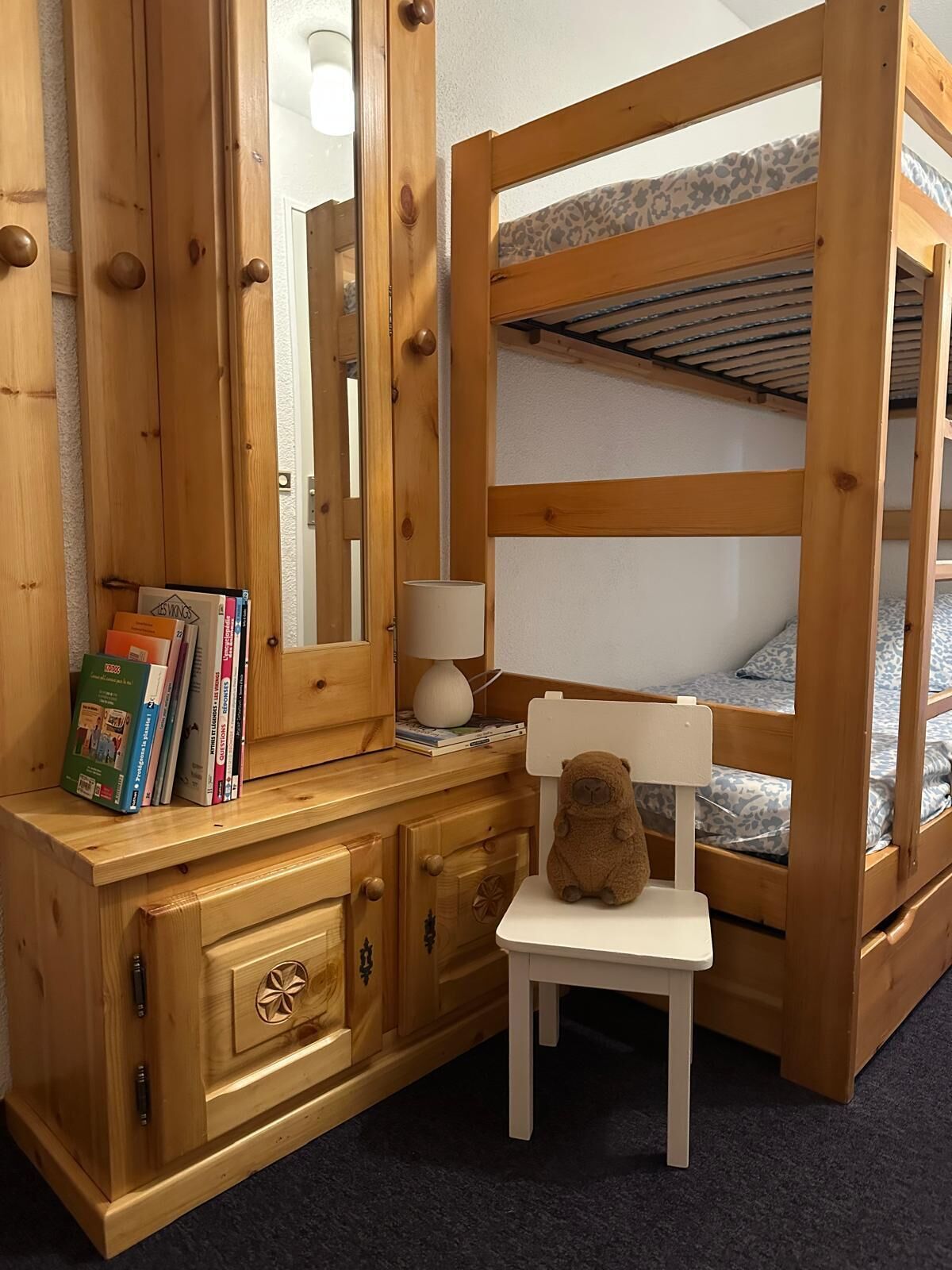 Una cama litera con estructura de madera, un escritorio pequeño con lámpara y una silla.