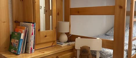 Una cama litera con estructura de madera, un escritorio pequeño con lámpara y una silla.